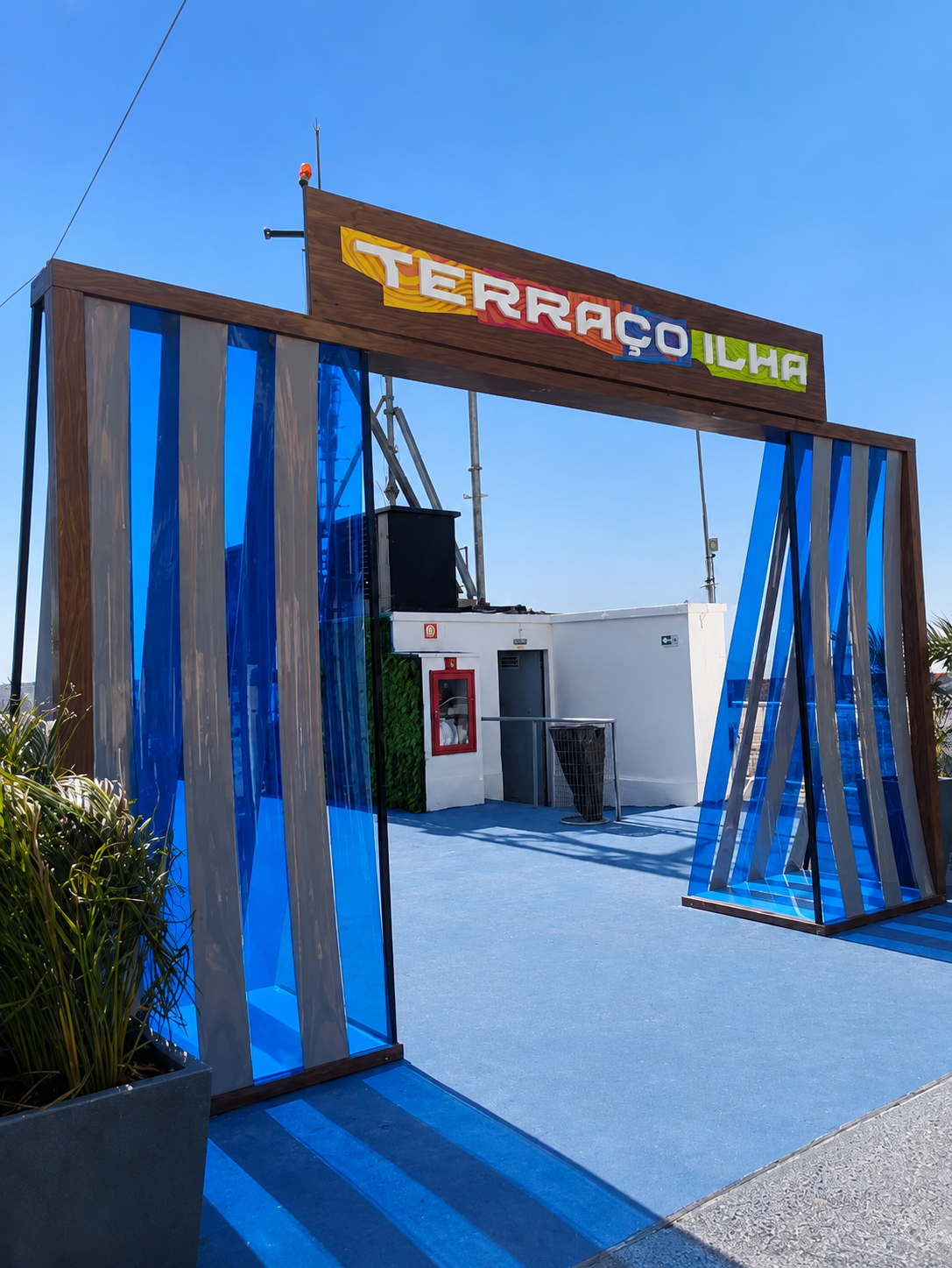 Pórtico de entrada Terraço Ilha Plaza — estrutura cenográfica em madeira e acrílico azul com letreiro suspenso