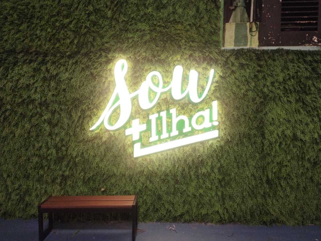 Letreiro luminoso Sou+Ilha sobre muro verde
