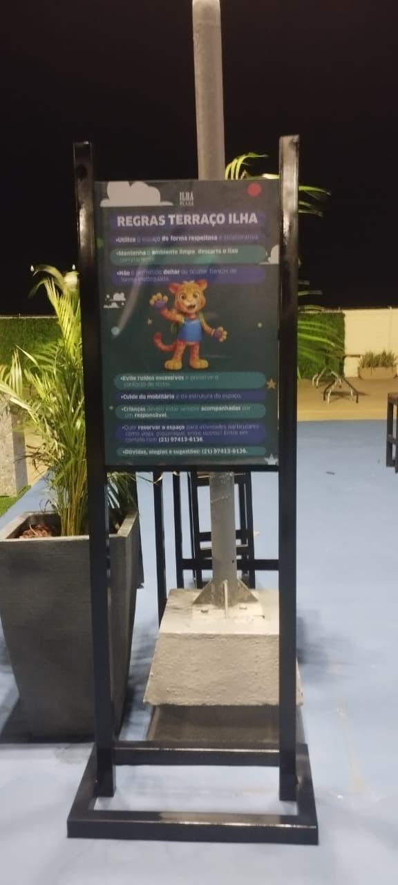 Totem Regras Terraço Ilha Plaza — sinalização noturna com mascote em área de lazer